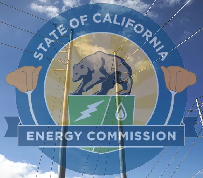 A circular sign for the California Energy Commission featuring the state seal with a grizzly bear, surrounded by blue border text reading "STATE OF CALIFORNIA." The sign shows energy-related imagery including a lightning bolt symbol and wind turbine, with power lines visible crossing the sky and clouds in the background.