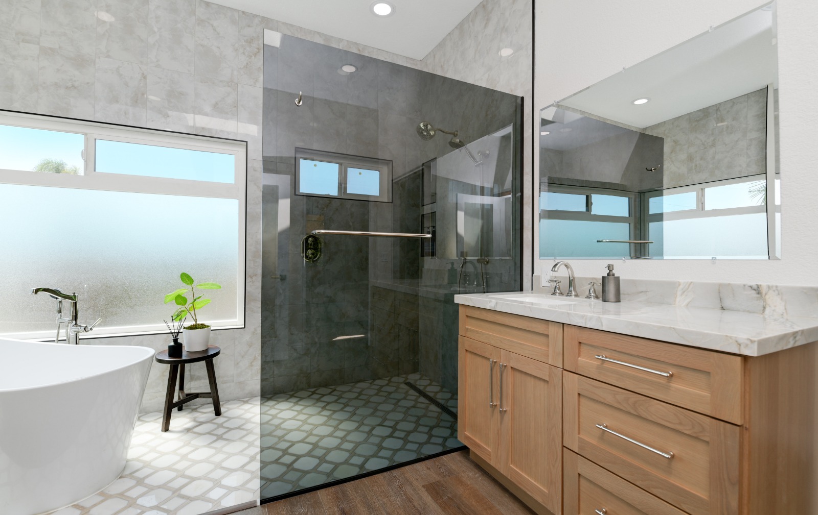 A modern luxury bathroom featuring a freestanding white soaking tub near a frosted window, a walk-in glass shower with dark gray tile walls, and a wooden vanity with white marble countertop. The space combines light marble-look wall tiles with geometric patterned floor tiles, creating an elegant contrast with the darker shower area. Natural light enters through strategically placed privacy windows, and the design emphasizes clean lines and contemporary fixtures.