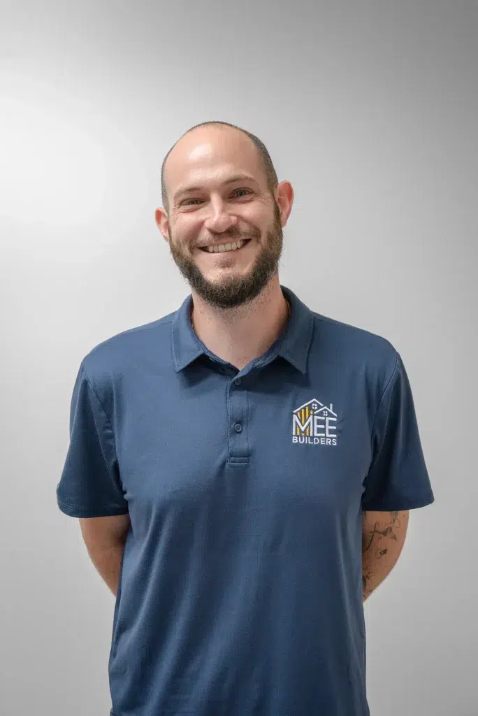 A smiling man with a beard and receding hairline wearing a navy blue polo shirt with the WFF Builders logo embroidered on the chest. He stands against a plain white background with his hands behind his back in a professional portrait style photograph. A tattoo is visible on his left forearm.