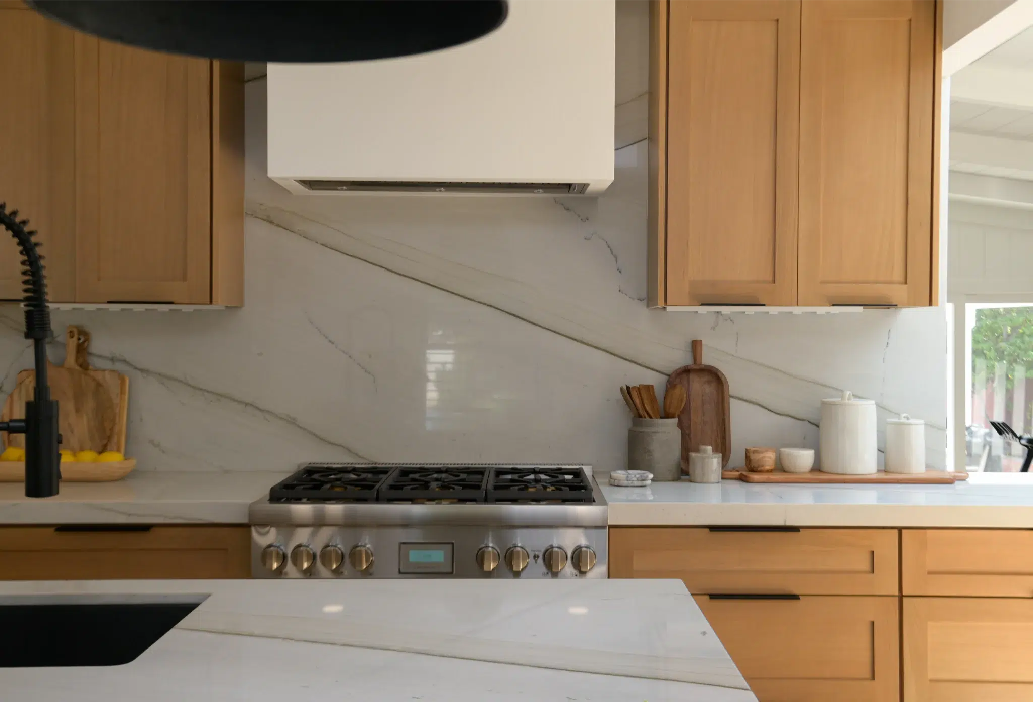 Warm-modern kitchen range wall with white oak cabinetry and quartz counters