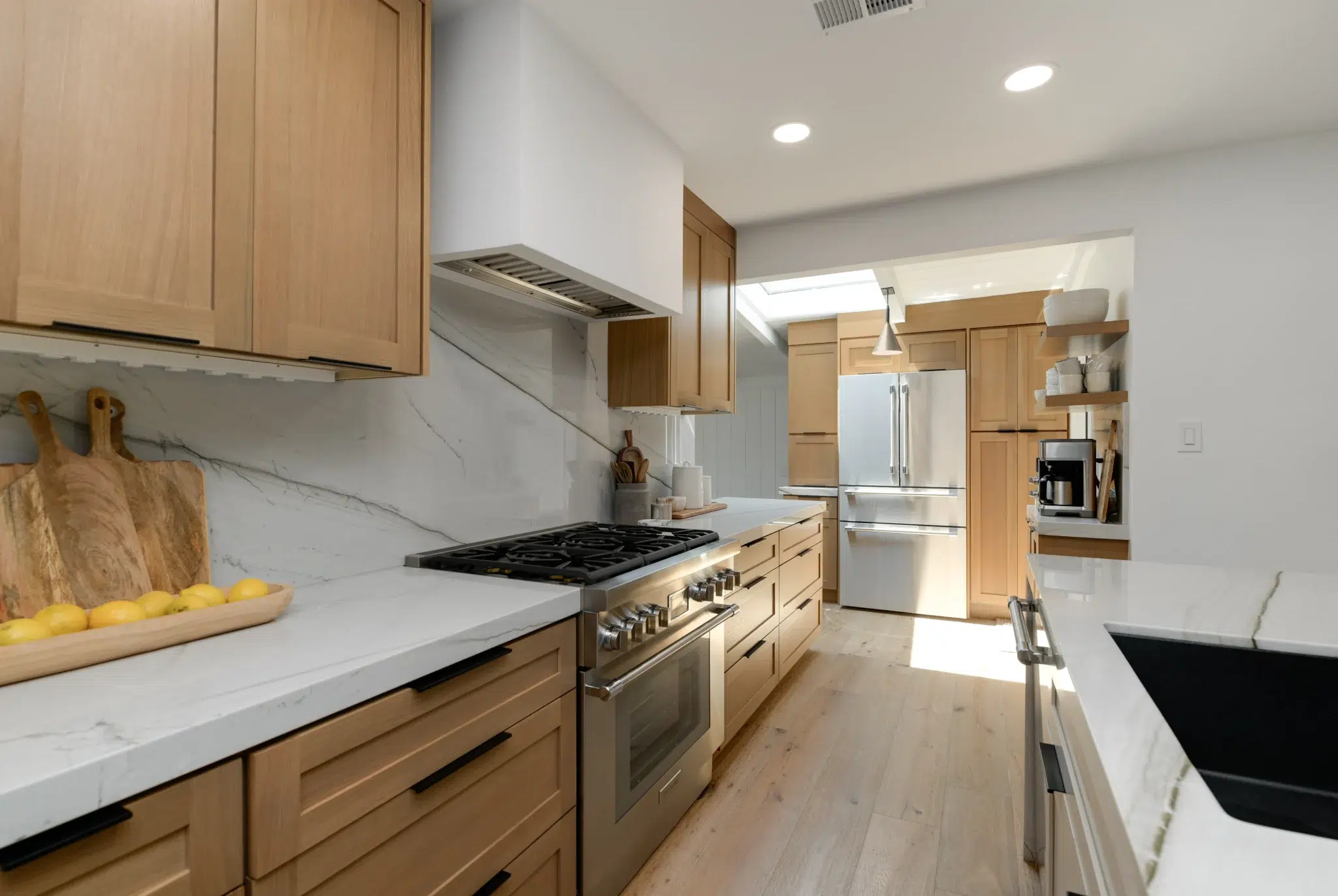 Stainless steel gas range beneath a full-height quartz slab backsplash in a remodeled kitchen