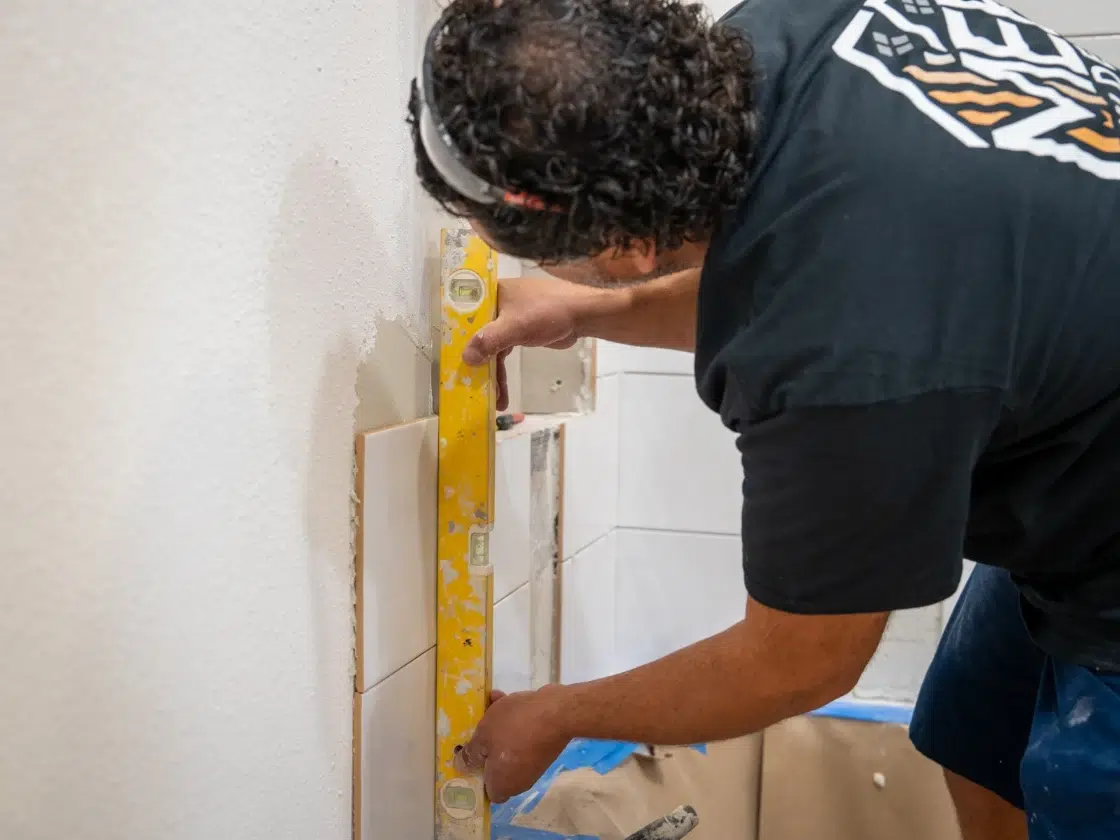 MEE Builders tile installer checking newly installed custom white bathroom wall tile with a level during a San Diego luxury spa remodel.