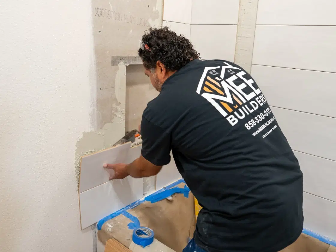 MEE Builders installer setting bright white wall tile in a San Diego luxury walk-in shower build.