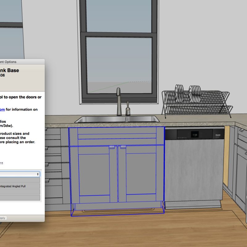 A SketchUp 3D model of a kitchen showing a KraftMaid sink base cabinet (model SB36) with its component options dialog box open. The dialog displays specifications including 24-inch depth, 34.5-inch height, and 36-inch width, with blue lines outlining the cabinet structure beneath the countertop. The kitchen scene includes gray cabinetry, a window above the sink, a dish rack, and a stove visible on the right side.
