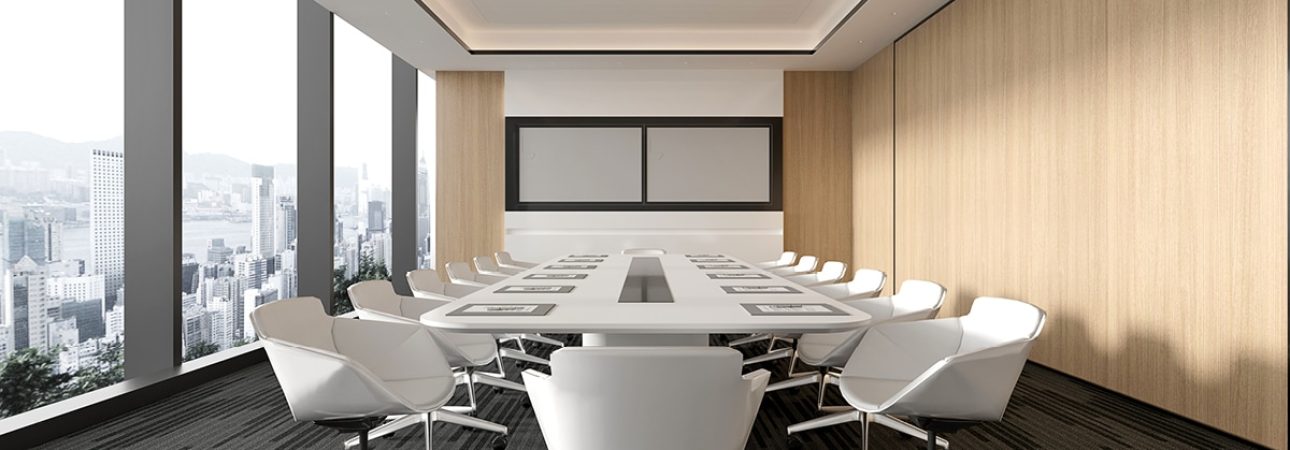 A modern corporate conference room with floor-to-ceiling windows offering panoramic city views. The space features a large white oval table surrounded by contemporary white swivel chairs, wood-paneled walls, and a minimalist design with recessed linear lighting in the ceiling. Two presentation screens are mounted on the back wall above the sleek wooden paneling.